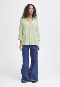 Camicia button-up verde chiaro con scollo a V e maniche a tre quarti abbinata a jeans cargo flared scuri e larghi, con tasche laterali.