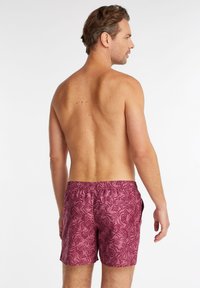 Shorts de bain rose foncé avec un motif de feuilles, taille élastique et poches latérales. Le tissu présente une texture lisse et légère.