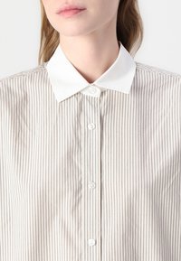 Gestreepte shirt in lichtbeige en wit, met een witte kraag, knoopsluiting aan de voorkant en verticale streepjes. Glad stof met een strakke afwerking.