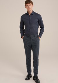 Camisa de botones azul marino de manga larga, combinada con pantalones oscuros de cuadros gris oscuro. Lleva zapatos de cuero negros. Diseño sencillo y ajustado.