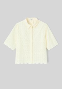 Blouse crème à manches courtes avec motif ajouré, bords festonnés, boutonnière sur le devant et col classique sur un fond uni.