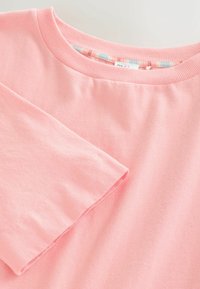 Haut à manches longues rose doux avec un col ras du cou côtelé et un doublure intérieure visible imprimée de fleurs à l'intérieur du col.