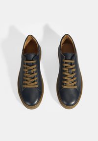 Marineblaue Leder-Sneaker mit strukturiertem Muster, braunen Schnürsenkeln und Gumm sole, ausgestattet mit einer runden Zehenpartie und minimalistischem Design.