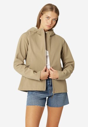 Beige softshell jacket with a hood, front zipper, and adjustable drawstrings, paired with blue denim shorts. Smooth, water-resistant fabric.