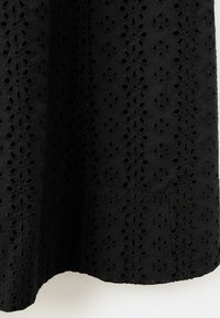 Tissu noir avec motif brodé floral découpé, drapé avec plis visibles et ourlet festonné.