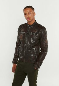 Veste de moto en cuir noir avec des accents matelassés aux épaules, des poches zippées et des écussons. Fini texturé et design ajusté.