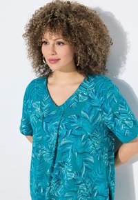 Blusa de manga corta en color aguamarina con escote en V y detalle de botones. Presenta un diseño con patrón de hojas en diferentes tonos de azul y blanco. Textura suave.