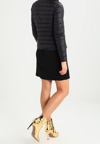 Doudoune noire avec des coutures horizontales, mini-jupe noire côtelée et bottines dorées brillantes à talons hauts avec un détail de fermeture éclair.