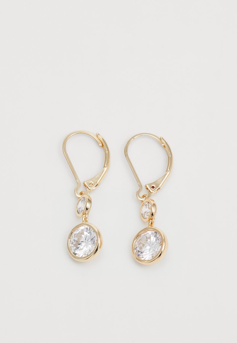 Brincos em tom de ouro apresentam duas pedras de cristal transparente, com corte oval e tamanhos diferentes, suspensas de um fecho de alavanca.