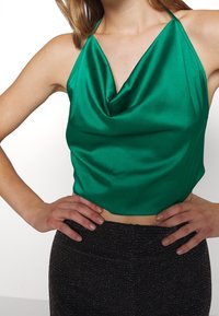 Haut à col licou en satin vert avec un décolleté drapé, un design court et une texture lisse, associé à un bas sombre et scintillant.