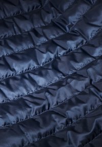 Dunkelblaues, gestepptes Gewebe mit einer glatten, glänzenden Oberfläche. Verfügt über diagonal genähte Paneele, die ein puffiges Aussehen erzeugen.