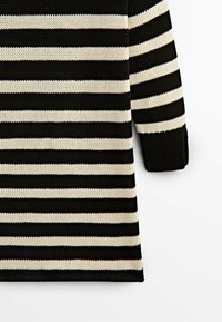 Svart och krämfärgad randig tröja med en lösstickad textur och trekvartsärmar, med växlande breda och smala ränder.