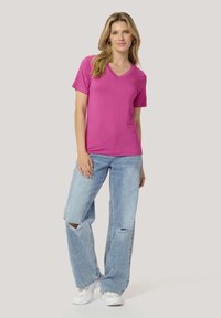 T-shirt fuchsia à col en V avec des manches courtes, associé à un jean bleu clair déchiré et des baskets blanches, offrant une coupe décontractée et une texture douce.