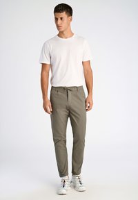 T-shirt léger en coton blanc, associé à un pantalon slim olive avec une taille élastique et un cordon de serrage.