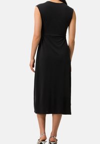 Czarna sukienka bez rękawów z dopasowanym korpusem i zwiewnym spódnicą w kształcie litery A, wykonana z miękkiego materiału. Oferuje subtelne marszczenie w talii.