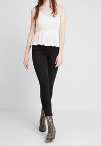 Top bianco a peplum con dettagli in pizzo, abbinato a jeans neri aderenti e stivaletti alla caviglia con stampa pitonata. Outfit semplice e casual in toni neutri.