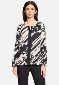 Trykt bluse med sort og creme farver, abstrakte blomster- og tekstmønstre, lange ærmer, rund halsudskæring og en detaljeret nøglehul.