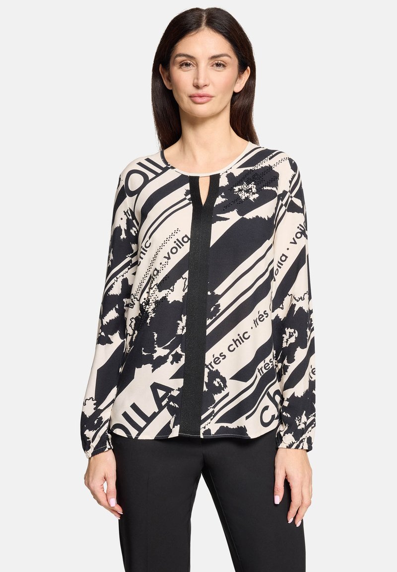 Trykt bluse med sort og creme farver, abstrakte blomster- og tekstmønstre, lange ærmer, rund halsudskæring og en detaljeret nøglehul.