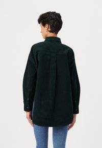 Camicia in velluto a coste verde scuro con piega sul retro, polsini con bottone e colletto classico, caratterizzata da una vestibilità rilassata e una texture morbida.