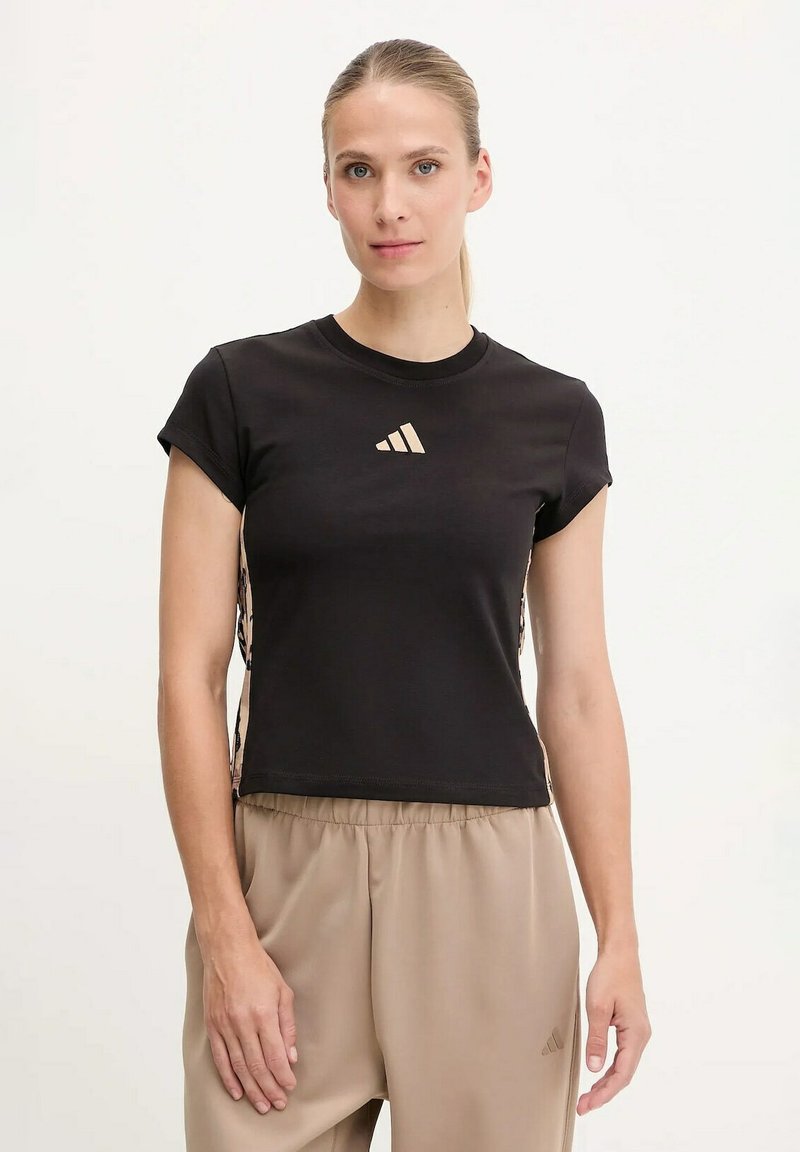 T-shirt nera a maniche corte con colletto rotondo, caratterizzata da un logo dorato sul petto e lati decorati. Abbinata a pantaloni beige.