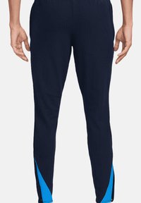 Pantaloni sportivi navy con costine verticali, design a gamba affusolata e accenti blu ai lati. Presentano una vita elasticizzata e una silhouette aderente.