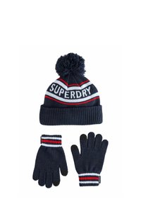 Námořnický modrý zimní set pletený s čepicí s bambulí, která má nápis "Superdry", a odpovídajícími rukavicemi s červenými, bílými a černými pruhovanými manžetami.