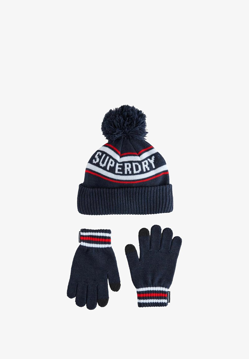 Zimski set u mornarsko plavoj boji koji uključuje pleteni šešir s pom-pomom na kojem je ispisan tekst "Superdry" te odgovarajuće rukavice s crvenim, bijelim i crnim prugama na manžetama.