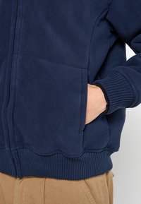 Marine fleece jacket met twee voorzakken, ribgebreide manchetten en zoom. Ritsluiting, zachte textuur en gladde stofafwerking.