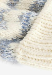 Écharpe tricotée en crème et bleu clair avec une finition douce et texturée. Dotée d'un fil lâche et épais avec de subtils accents scintillants.