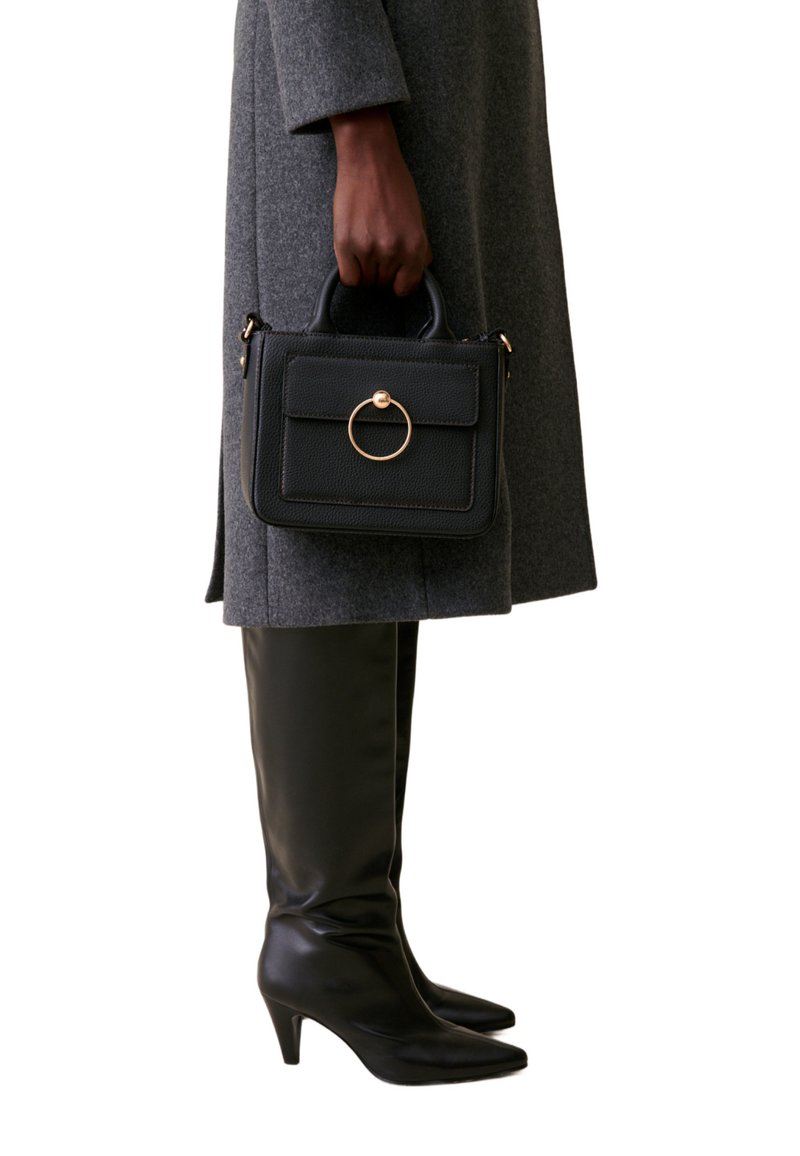 Sac en cuir noir avec une finition texturée, détail en métal doré en forme de cercle et poignées supérieures, associé à des bottes noires montant jusqu'aux genoux.