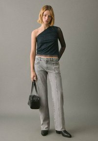 Asymmetrisches dunkles Oberteil mit transparentem schwarzen Ärmel; hellgraue gerade Jeans; schwarze Handtasche; Stiletto-Ankle Boots. Einfaches, elegantes Design.