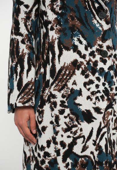 Πλεκτό παλτό με έντονο αφηρημένο σχέδιο σε τιρκουάζ, καφέ και λευκό. Έχει χαλαρή γραμμή, μακριά μανίκια και πέντε μαύρα κουμπιά.