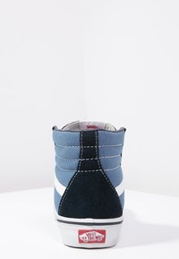 Wysokie trampki z niebieskiego i czarnego zamszu oraz płótna. Białe paski po bokach i logo Vans na czerwonej pętli na pięcie. Wyś cushioning wokół kołnierza.