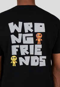 Černé tričko s velkými šedými blokovými písmeny, která hlásají "ŠPATNÍ PŘÁTELÉ", s oranžovými a žlutými akcenty v podobě kreslených panenek po stranách.