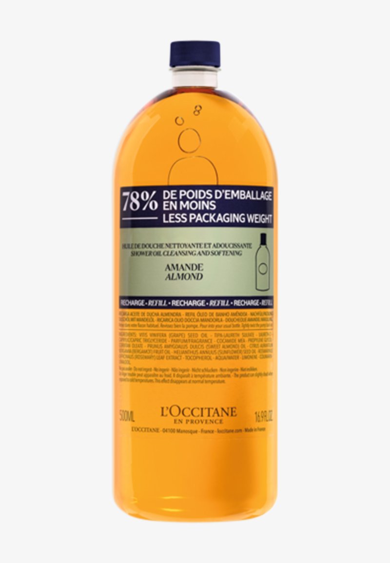 Bottiglia di plastica trasparente di olio da doccia all'amaretto, 500 mL, con tappo blu, liquido arancione e un'etichetta bilingue con dettagli sul prodotto.