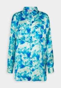 Blusa blu tie-dye con colletto, maniche lunghe, due tasche frontali e chiusura con bottoni. Realizzata in morbido tessuto di satin con uno sfondo chiaro.
