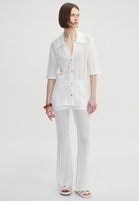 Witte gebreide outfit bestaande uit een kortomarm, knoopsluiting cardigan met een kraag en bijpassende uitlopende broek, beide met een gestructureerd patroon.