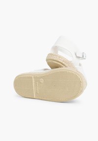 Sandale en tissu blanc avec sangle ajustable, semelle intermédiaire en jute tressé et semelle extérieure en caoutchouc texturé. Les détails incluent le logo sur la semelle.