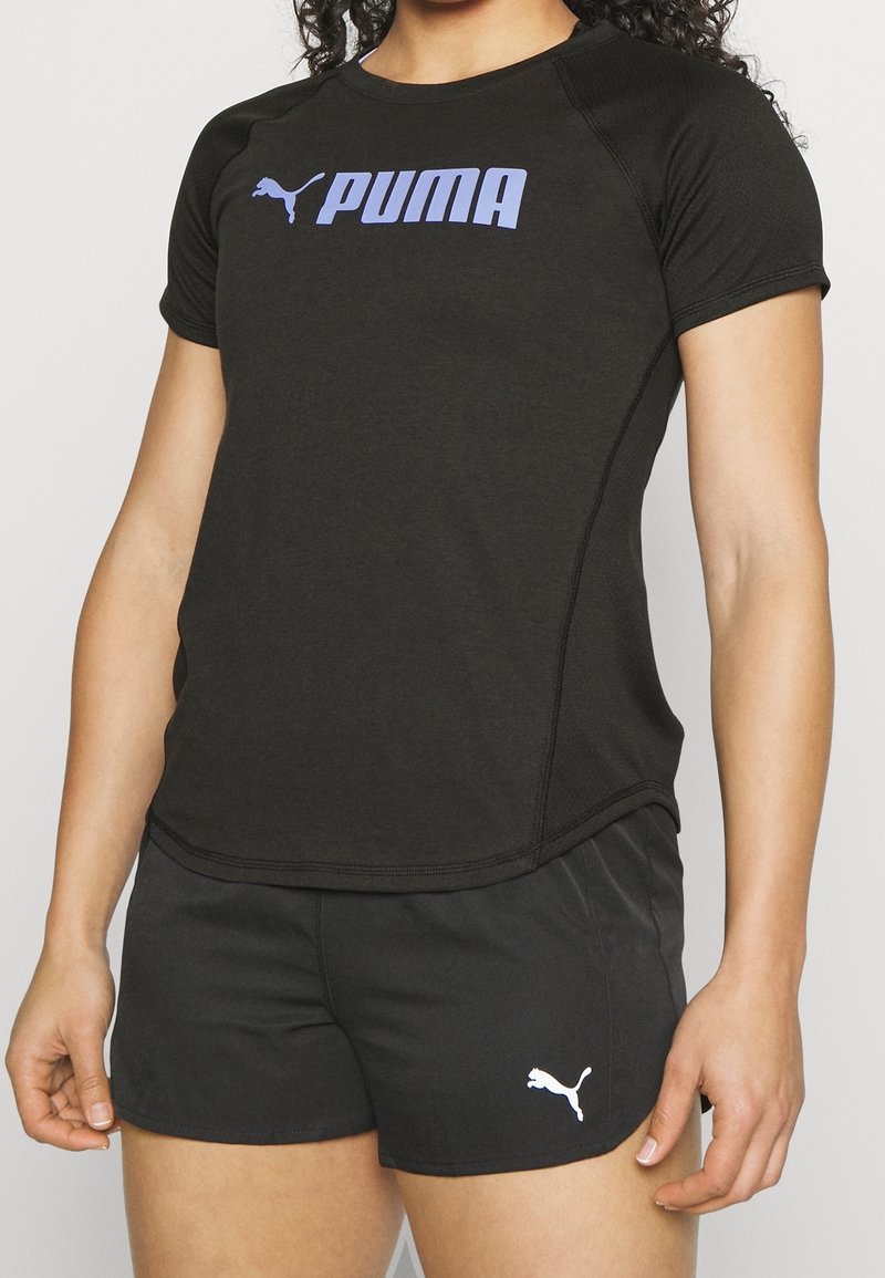 Černé sportovní tričko s krátkým rukávem, se zlaceným logem "PUMA" v purpurové barvě. V kombinaci s černými šortkami, na kterých je také bílé logo PUMA.