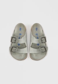 Γκρίζες σουέτ σάντες με δύο ρυθμιζόμενους ιμάντες και μεταλλικές αγκύλες. Οι εσωτερικές σόλες φέρουν μπλε λογότυπα και σηματοδοτήσεις μεγέθους. Επιφάνειες από καουτσούκ.