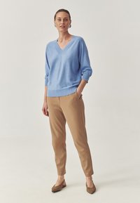 Pulover tricotat de culoare albastru deschis, cu decolteu în V, mâneci trei sferturi, asortat cu pantaloni tapered de culoare bej și mocasini maro cu vârf ascuțit. Textură netedă.