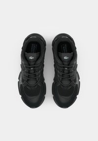 Zapatillas deportivas negras con parte superior de malla y sintético, cordones, cuello acolchado y suela de goma. Presenta un logo sutil en la lengüeta.