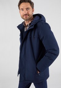 Cappotto isolato blu navy con cappuccio, tasche con zip e chiusura a bottoncini. Presenta una texture morbida e un design su misura.