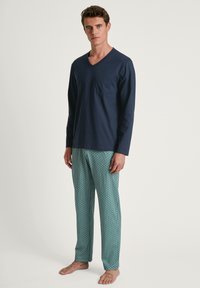 Marineblauwe longsleeve V-hals t-shirt met een borstzak en groene loungebroek met een geometrisch patroon. Gemaakt van een katoenmix, met een relaxte pasvorm.