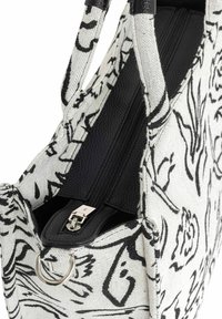 Biała torba na ramię z płótna z czarnymi wzorami kwiatowymi, z teksturowanym czarnym zamkiem błyskawicznym z syntetycznej skóry, okuciami i podszewką wewnętrzną.