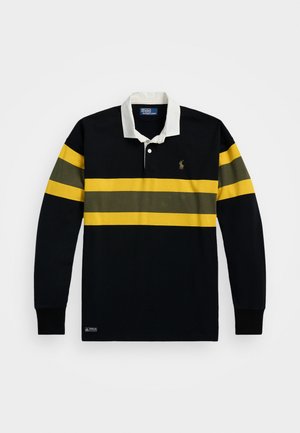 Koszula polo z długim rękawem w kolorze granatowym z białym kołnierzykiem i poziomymi paskami w kolorze żółto-zielonym. Posiada logo na lewej piersi oraz ściągacze przy rękawach.