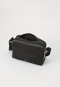 Geantă crossbody din nailon negru, cu un compartiment principal cu fermoar, curea ajustabilă și accesorii din argint. Textură netedă, design minimal.