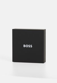 Svart rektangulær boks med matt overflate, med den hvite "BOSS"-logoen sentrert på forsiden. Enkel og kompakt design.