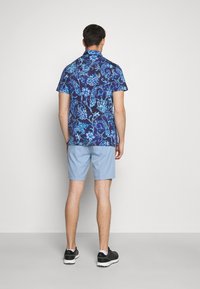 Košile s krátkým rukávem modré barvy s květinovým vzorem na tmavě modrém pozadí, doplněná světle modrými šortkami. Černé sportovní boty dotvářejí celý vzhled.