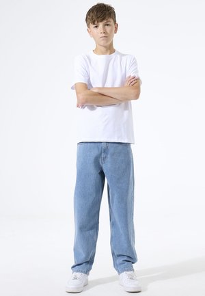 Camiseta blanca de algodón con mangas cortas, combinada con vaqueros de mezclilla azul claro y de corte holgado, y zapatillas blancas. Diseño sencillo sin estampados.